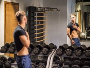 Young Shirtless Handsome Muscular Man Admiring His Muscles in Gym Mirror or Checking Progress and