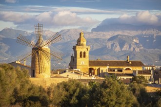 Village with windmill and church in front of mountains under a cloudy sky, Algaida, Majorca, Spain,