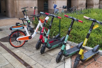 MILAN, ITALY, AUGUST 4, 2021: colorful rental scooters and bicycles on a sidewalk in the city