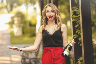Happy young attractive white woman laughing joyfully, talking on the phone, holding a bottle of