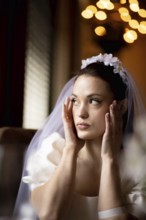 Bride looking sideways, hands on cheeks, with warm bokeh lights in the background