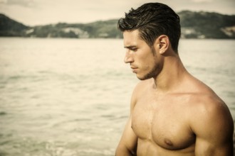 Attractive young man in the sea getting out of water with wet hair, looking away to a side