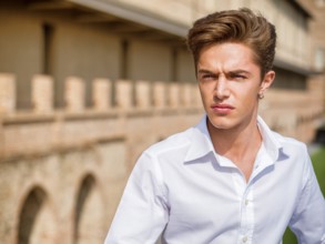 One handsome elegant young man in urban setting in European city, standing in sunny day