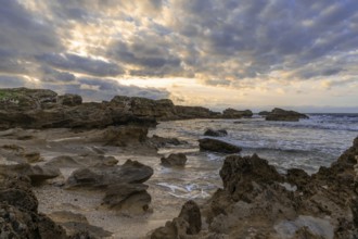 A rocky cove and sandy beach under an expressive sunset sky on the rugged west coast of Sardinia