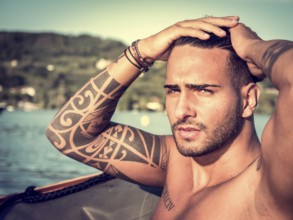 Portrait of young bearded handsome man with tattooed body looking sexually at camera sailing in