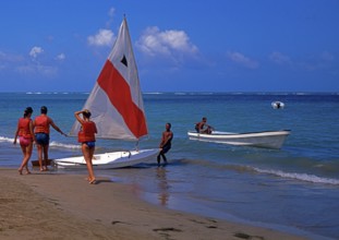 Beach, helper pulls sailboat into the water for 3 tourists, Playa Dorada, Dominican Republic,