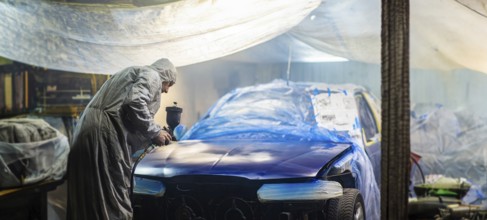 Person in protective suit spray painting a car in a dimly lit garage