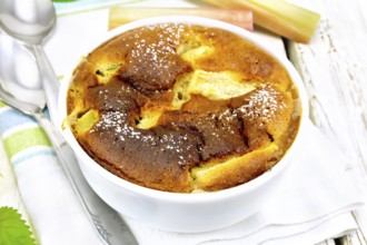 Pie klafouti with rhubarb in the bowl, mint and rhubarb stalks on a towel on the background of
