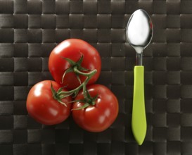 Three red tomatoes in the same one branch with a vibrant green spoon
