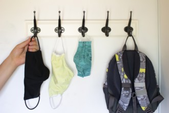 A person about to get a face mask form a Wall Hook or Coat Rack on a white wall
