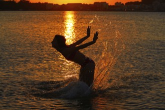 Girl splashing water with hands at sunset beach in orange sky
