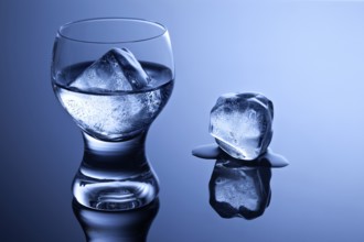 An elegant shot glass with vodka and ice and a melting ice cube on a reflective surface