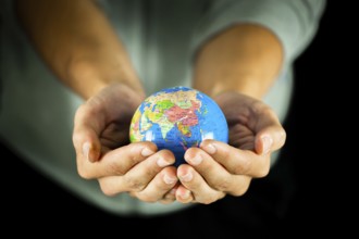 Male hands holding the Earth globe on black background