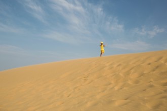 A tourist girl in a yellow dress runs along a sandy dune in the desert. Travel, sights of Dagestan,