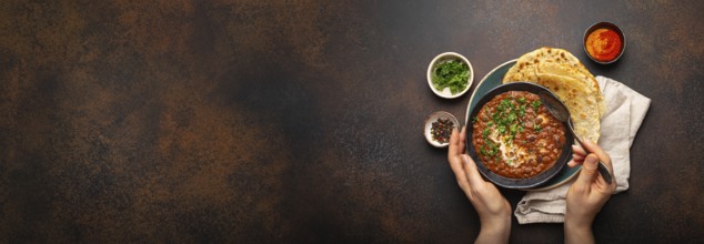 Female hands holding a bowl, eating traditional Indian Punjabi dish Dal makhani with lentils and