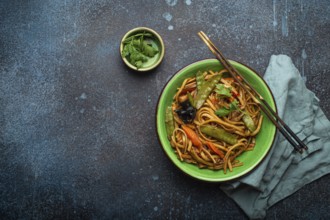 Asian stir fry udon noodles with chicken, vegetables, mushrooms in green ceramic bowl with wooden