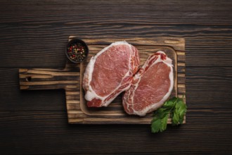 Cut raw meat pork steaks with seasonings on kitchen cutting board, rustic wooden background top
