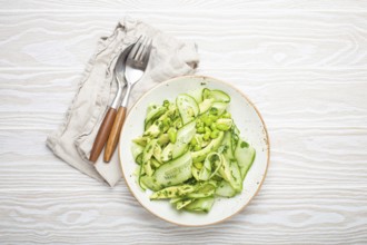 Healthy vegan green avocado salad bowl with sliced cucumbers, edamame beans, olive oil and herbs on