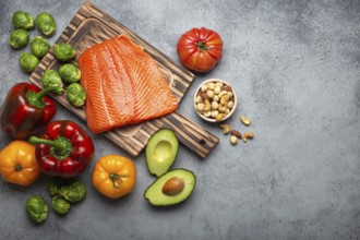 Fresh raw salmon fillet on wooden cutting board, organic bio vegetables and nuts on rustic stone