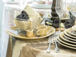 Set of new dishes on table with tablecloth. Stack of beige plates and wine glasses on restaurant
