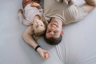 Smiling dad with little daughter lie on the bed upside down.
