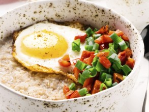 Savory oatmeal in craft trendy bowl, served with vegetables and fried egg on white concrete