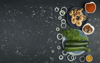 Fresh zucchini, mushrooms, spices and herbs on a black board. View from above. Copy space
