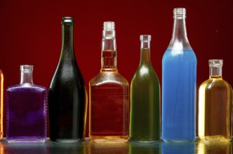 Verschiedene alkoholische Getränke in transparenten Flaschen auf rotem Hintergrund