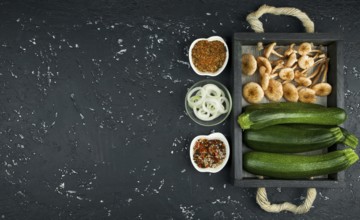 Fresh zucchini, mushrooms, spices and herbs on a black board. View from above. Copy space