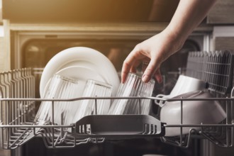 Female hand loading dished, empty out or unloading dishwasher with utensils. Kitchen appliances,