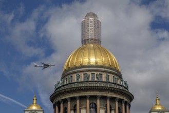 Historic building with golden dome and a passing aeroplane in the blue sky with clouds, saint