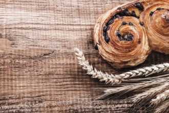 Roll with raisins wheat ears on oak wooden board food and drink concept