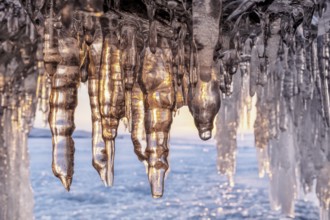 Ice cave on Baikal lake in winter. Blue ice and icicles in grotto in the sunset sunlight. Olkhon