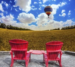 Huge balloon flies over a field. Convenient red chairs in a wheat field. The concept of eco-tourism