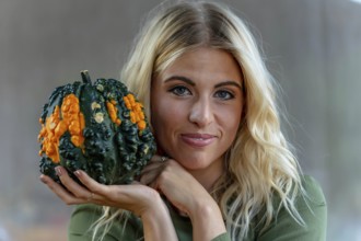 A stunning blonde model poses in a vibrant pumpkin field, wearing a stylish autumn outfit with a