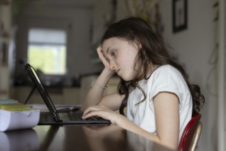 Girl, 10 years old, sits at the table with a tablet and learns
