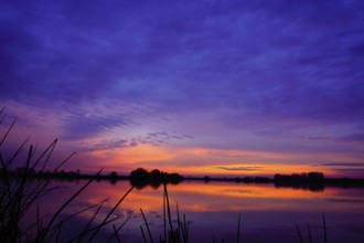 Purple and orange sky over a calm lake at dawn, Polder 27798 Hude-Germany