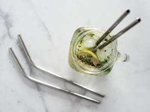 Metal drinking straws and cold drink in glass mason jar on white marble background. Top view or