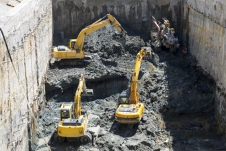 Excavators dig at a construction site of a street and a subway. Baggers transport dirt to a higher