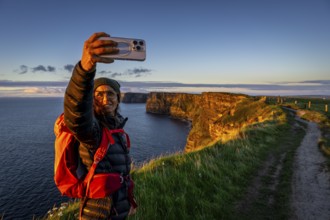 Female hiker taking a selfie, Cliffs of Moher, The Burren, County Clare, Ireland, United Kingdom,