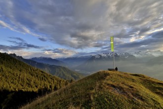 Sitting woman enjoying a dreamlike evening mood in the mountains, view to the Rätikon, flag of the