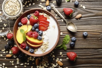 Flat lay of fruit healthy muesli with peaches strawberry almonds and blackberry in clay dish with