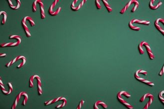 Christmas sweets frame with mini candy canes in red and white stripes, on a green paper background