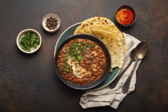 Traditional Indian Punjabi dish Dal makhani with lentils and beans in black bowl served with naan