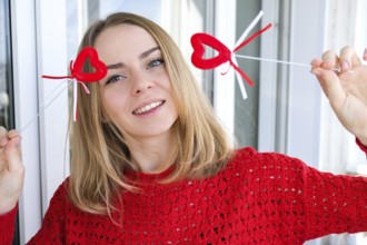Young blonde girl in red sweater holding red hearts showing emotions. Taking selfie. Video chat.