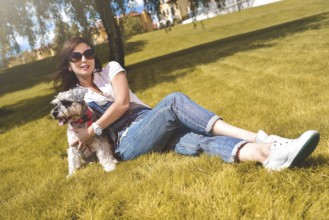 Pretty adult caucasian happy woman resting in the park on a sunny day with her beloved dog. Female