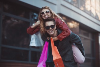 Happy couple shopping together and having fun. Boyfriend carrying his girlfriend on the piggyback