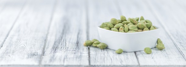 Wasabi coated Peanuts as high detailed close-up shot on a vintage wooden table (selective focus)