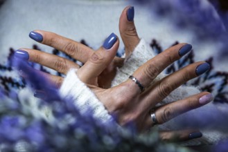 Hands showing purple manicure resting on a soft sweater, with a hint of floral elements