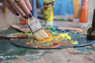 A detailed closeup of a hand skillfully mixing together vibrant and colorful paints on a palette
